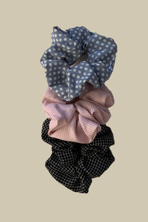 his set includes three soft fabric scrunchies in light pink, light blue, and classic black, each adorned with delightful white stripes or polka dots.