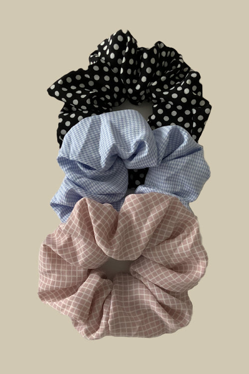 his set includes three soft fabric scrunchies in light pink, light blue, and classic black, each adorned with delightful white stripes or polka dots.